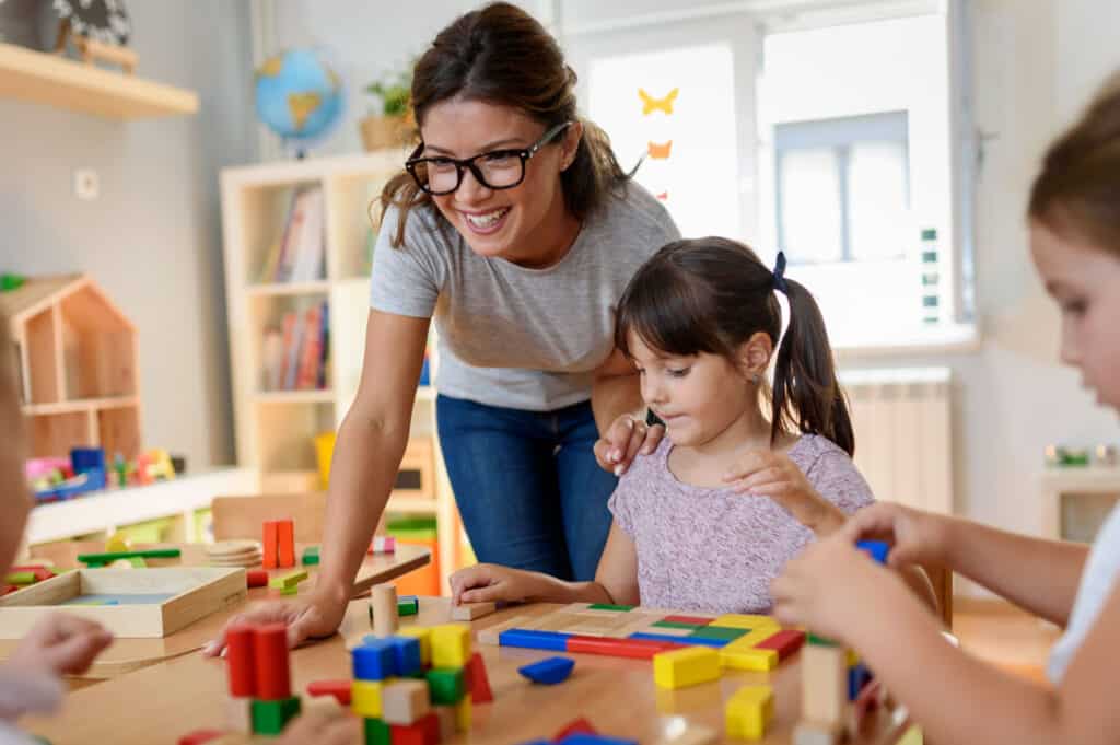 Happy teacher playing with children in a preschool classroom with educational toys.