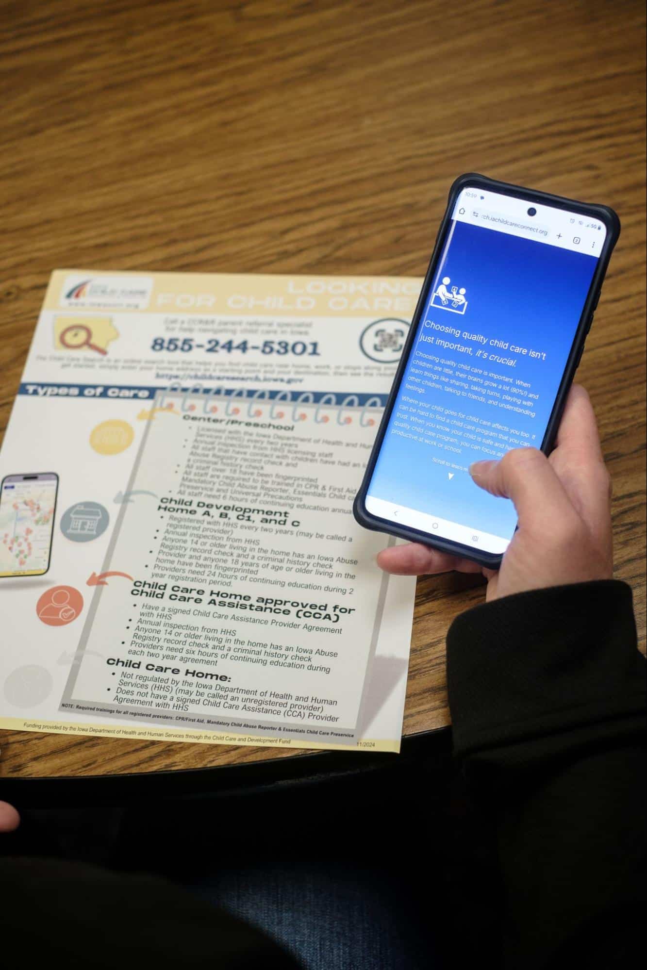 Person using smartphone to access Iowa Childcare Resource & Referral information on a table.