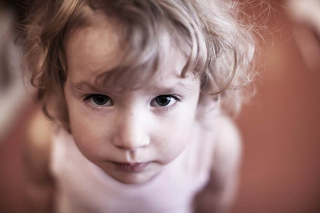 Close-up of a young child with curly blonde hair and blue eyes looking up.