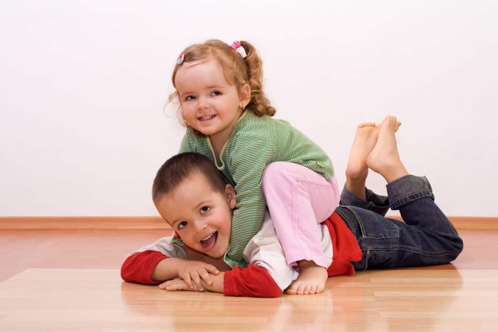 Happy brother and sister playing wrestling on the floor