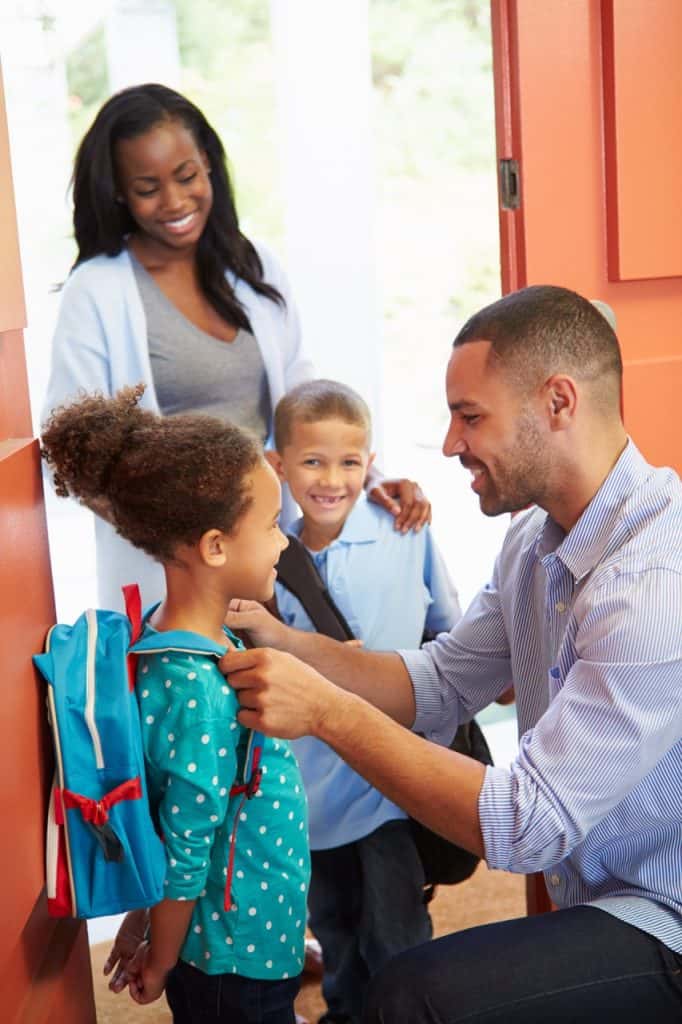 Child greeting a man at the door with a woman and two children in the background.