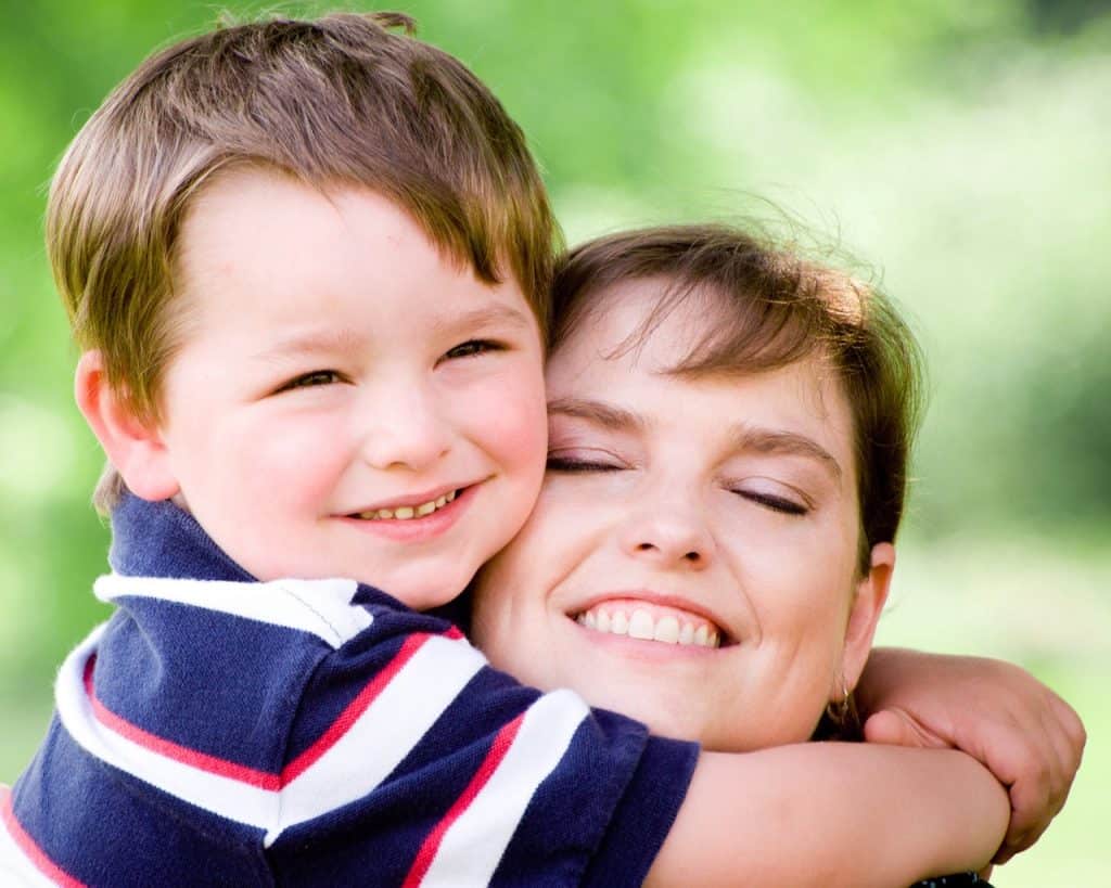Happy child hugging caregiver outdoors, promoting child care and mental health.