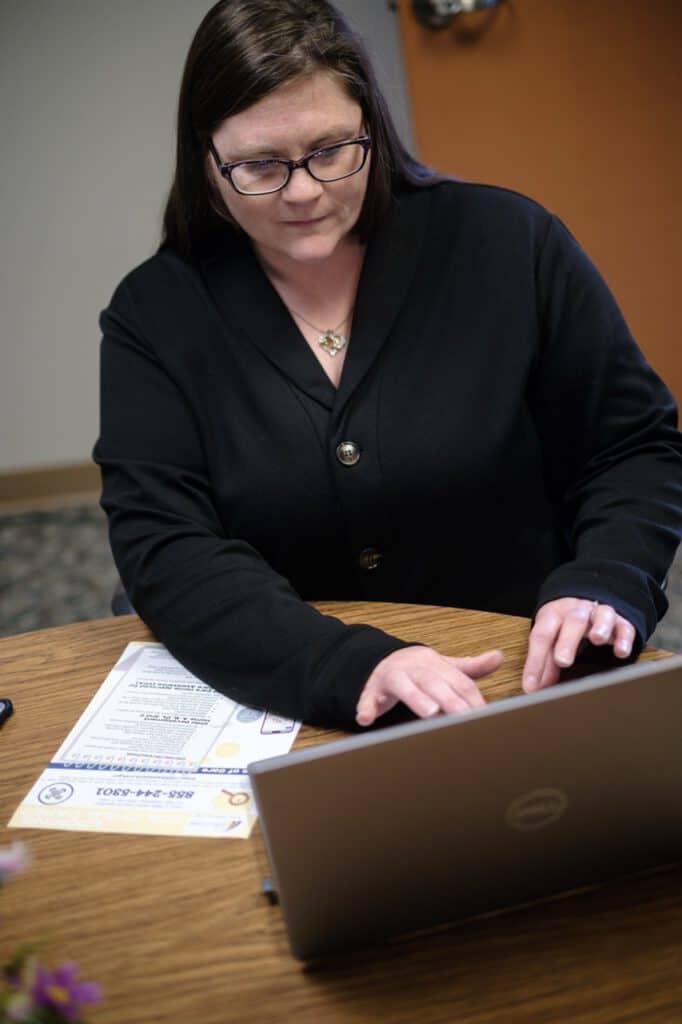 Woman working on a laptop at a desk with documents in an office setting.