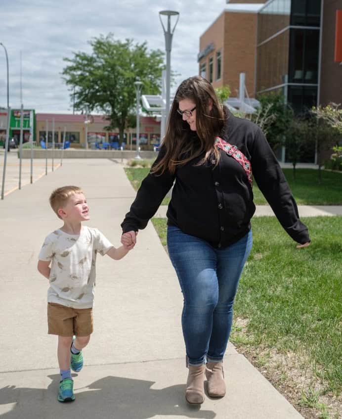 Woman holding child's hand while walking outdoors near a modern building.