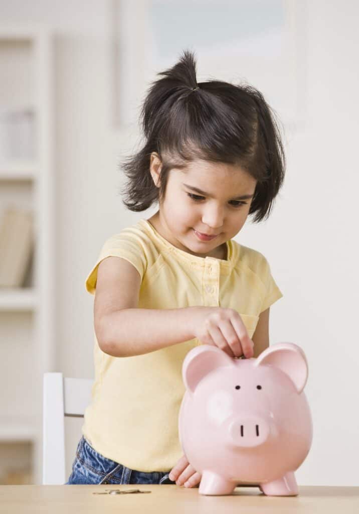 Young girl saving money in a pink piggy bank at home.