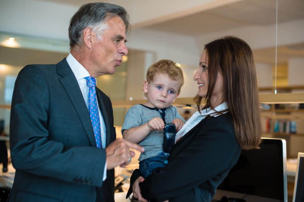 Businessman talking to woman holding a child in an office setting.