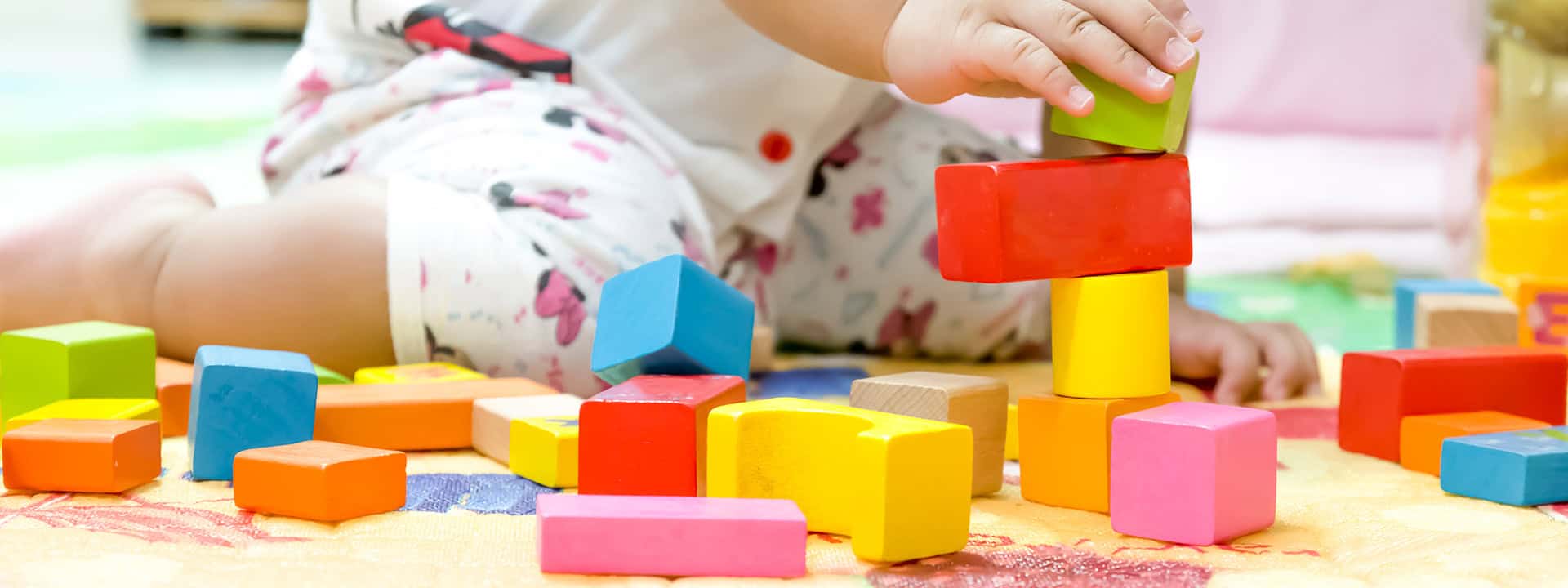 Child playing with colorful building blocks on a soft surface.