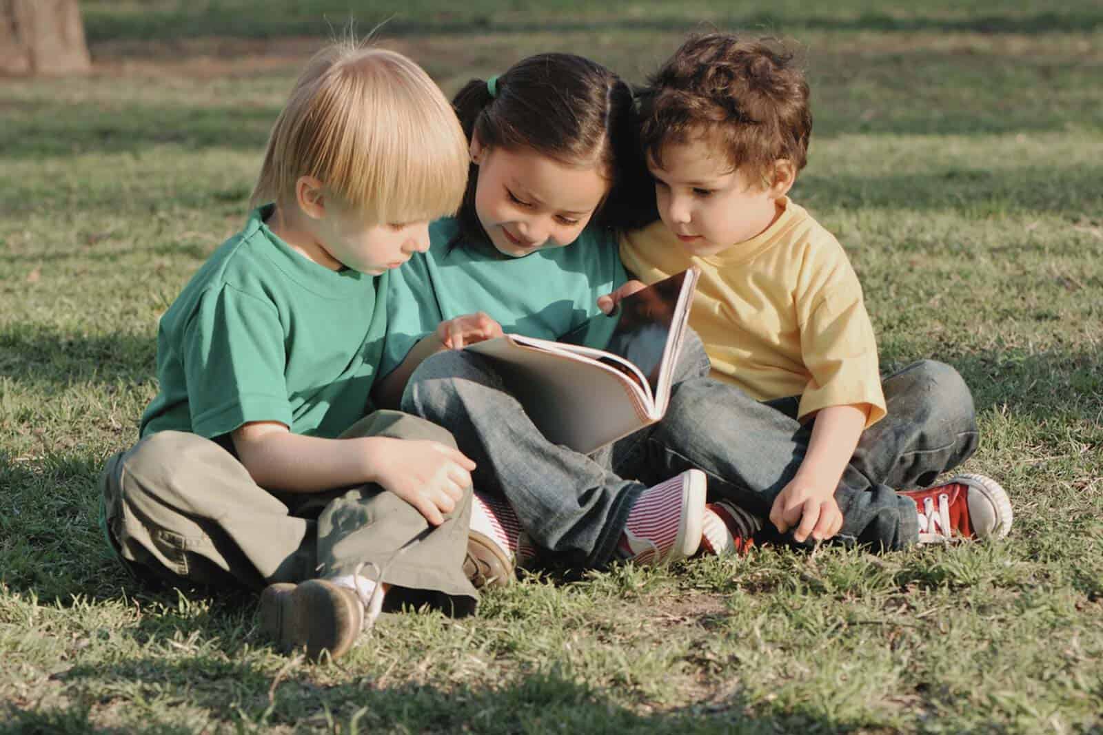 Children reading a book outdoors in a grassy area for child care learning.