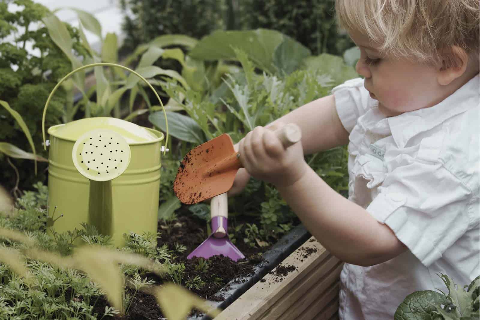 Child planting in a garden with watering can and gardening tools.