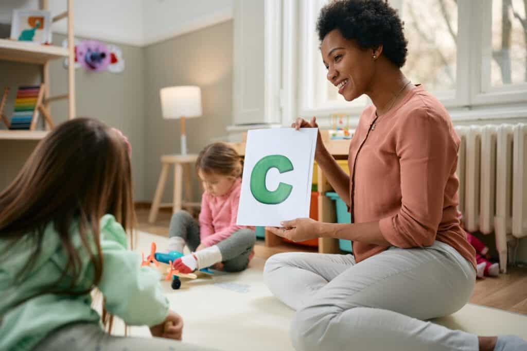 Happy African American teacher holding letter C while teaching kids the alphabet at kindergarten.