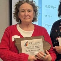 Two women at Iowa CCR&R event, one receiving leadership award, in front of schedule screen.