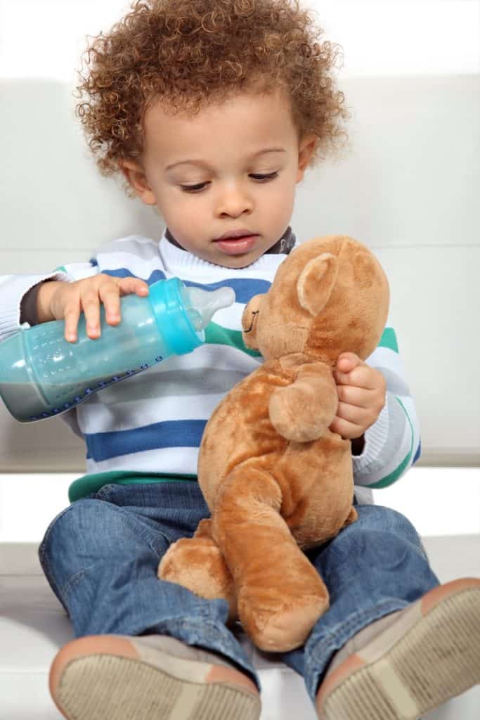 Little boy feeding teddy bear from bottle