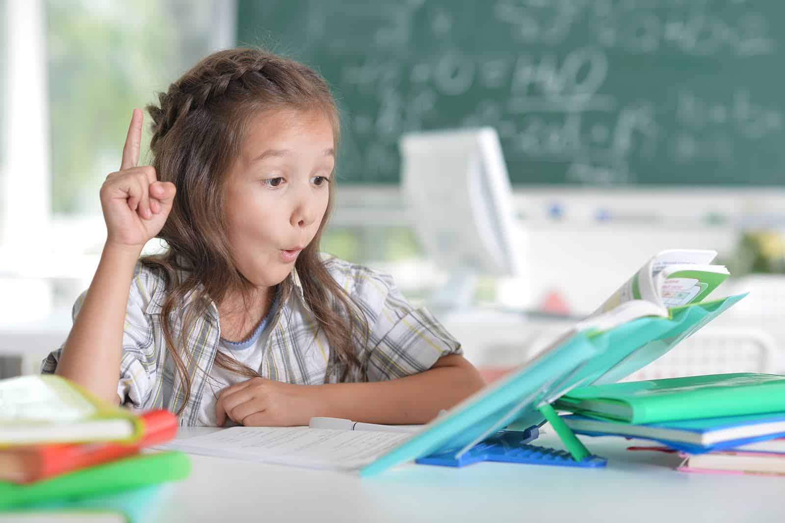 Young girl studying with books and a tablet in classroom setting.