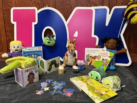 Children's toys and books displayed on a table with a large 'Iowa' sign in the background.